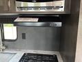A 2021 Jayco Jay Flight kitchen area featuring a stovetop with two burners below a built-in microwave and a black range hood with control buttons