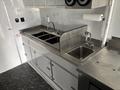 A stainless steel countertop with three sink basins and faucets inside a mobile kitchen space
