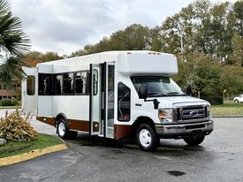 A 2014 Ford Econoline shuttle bus with a white and brown exterior and an open door, showcasing its spacious interior layout