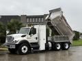 A 2011 International 7500 dump truck with its bed raised, revealing a silver metal dump body and equipped with a side compartment for tools or equipment