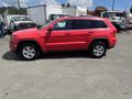 A red 2015 Jeep Grand Cherokee is parked facing sideways showing its four-door design and alloy wheels