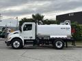 A white 2025 Peterbilt 536 water truck with a cylindrical water tank and red hosing on the side
