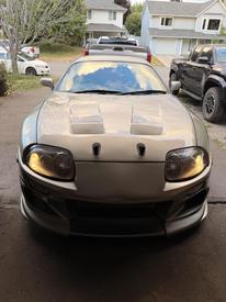 A 1997 Toyota Supra with a sleek design and distinctive hood vents is displayed prominently in the foreground showcasing its headlights and sporty front bumper