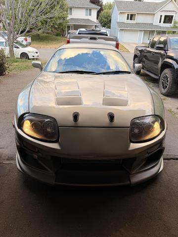 A 1997 Toyota Supra with a sleek design and distinctive hood vents is displayed prominently in the foreground showcasing its headlights and sporty front bumper