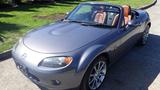A 2007 Mazda Miata with a sleek gray exterior and a tan leather interior parked with the top down
