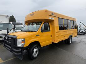 A yellow 2021 Ford Econoline bus with large windows and a front grille guard parked at a location