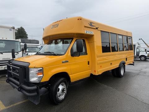 A yellow 2021 Ford Econoline bus with large windows and a front grille guard parked at a location