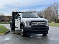 A 2017 Ford F-450 Super Duty truck with a flatbed and black side panels parked on a wet surface