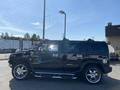 A black 2003 Hummer H2 is parked with shiny chrome wheels and a prominent front grille