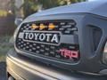 A close-up of the front grille of a 2004 Toyota Tacoma featuring the Toyota logo and TRD emblem with orange lights on the top of the grille