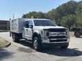 A 2019 Ford F-550 pickup truck with a silver body and a utility bed featuring a side-mounted compartment and an orange roof light