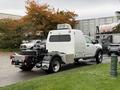 A 2024 RAM 5500 truck with a white cab and a flatbed rear is parked, featuring a compact storage compartment and a mounted power generator on top