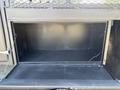 An open storage compartment of a 2005 GMC C7500 Topkick with a metal interior and a grid-patterned door