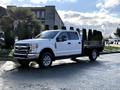 A white 2020 Ford F-350 pickup truck with a flatbed, featuring four doors and chrome accents, parked on a pavement with a well-defined profile