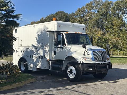 A white 2008 International 4400 truck with an enclosed cargo area and an orange light on top parked on a street
