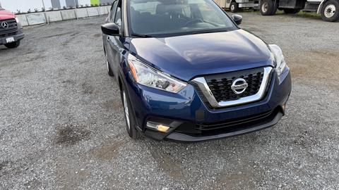 A blue 2019 Nissan Kicks facing slightly towards the viewer with its headlights on and the Nissan logo prominently displayed on the front grille