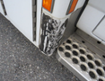 A close-up view of the corner of a 2011 Chevrolet Express showing scuff marks and scratches on the white exterior near the step area