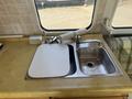 A kitchen sink area in a 1976 GMC Motorhome featuring a stainless steel sink with a faucet and a cutting board next to it on a yellow countertop