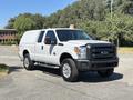 A white 2014 Ford F-250 SD with a black front grille and chrome wheels parked on a street