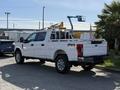 A white 2021 Ford F-250 Super Duty truck with a ladder rack in the bed is parked with its rear side facing the viewer