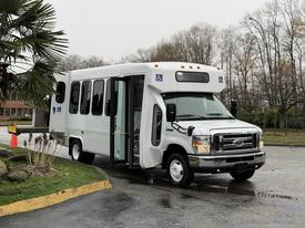 A 2017 Ford E450 shuttle bus with a white exterior and accessible features parked at an angle with its side door open
