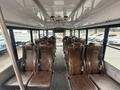 Interior of a 2021 Ford Econoline bus featuring rows of brown leather seats with seatbelts and no passengers