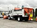 A 2012 International 7400 truck equipped with a large orange plow at the front and a salt spreader attached to the back
