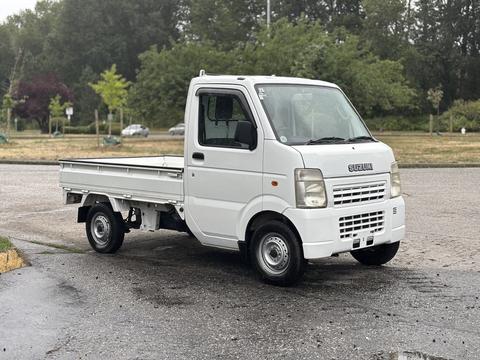 A white 2008 Suzuki Carry truck with a flatbed design and a compact cabin is parked at an angle
