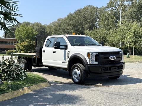 A 2018 Ford F-550 truck with a flatbed design is parked, featuring a white exterior and an orange light on the roof