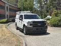 A white 2019 Ford F-150 pickup truck with a full cab and a ladder rack on top parked on a paved path