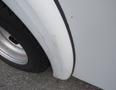 A close-up view of the wheel arch area of a 2011 Chevrolet Express showing a scuffed white surface and part of the tire