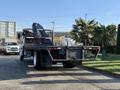 A 2015 Hino 358 truck with a flatbed and hydraulic lift system parked prominently, featuring a solid black chassis and visible rear lights