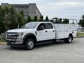 A white 2020 Ford F-550 with a utility body and dual rear wheels parked with tool compartments on both sides