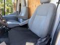 Interior of a 2015 Ford Transit showing two gray cloth seats with adjustable armrests and a simple dashboard design