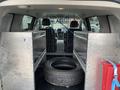 The interior of a 2014 RAM Cargo Van featuring metal shelves on each side a spare tire in the center and a metal grid separating the front seats from the cargo area