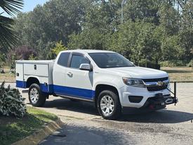 A white 2017 Chevrolet Colorado with blue accents parked on a driveway with a truck bed cover and a trailer hitch attached