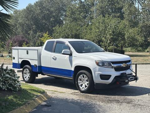 A white 2017 Chevrolet Colorado with blue accents parked on a driveway with a truck bed cover and a trailer hitch attached