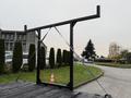 A black metal frame with an overhead support beam and diagonal braces stands on a flatbed truck