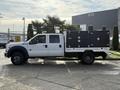 A white 2015 Ford F-550 truck with a black flatbed and toolboxes on the sides parked on a concrete surface
