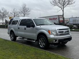 A silver 2014 Ford F-150 parked with a chrome front grille and alloy wheels featuring a truck bed cap and side steps