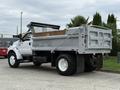 A white 2004 Ford F-750 dump truck with a silver cargo bed in the raised position