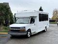 A 2015 Chevrolet Express shuttle bus with a white exterior and large windows parked on a driveway