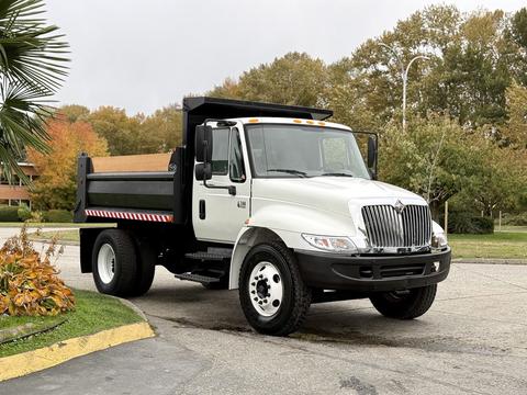 A 2006 International 4200 dump truck in white with black accents and a wooden bed parked on a street