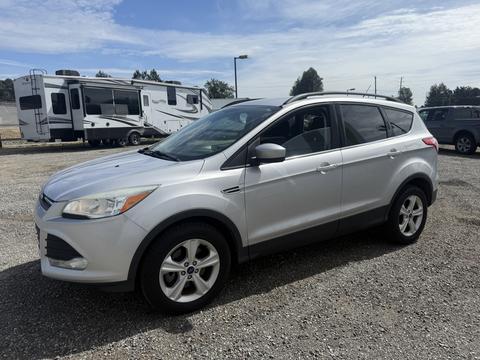A silver 2014 Ford Escape parked on gravel with a side view showcasing its sporty design and five-spoke wheels
