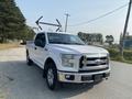 A white 2016 Ford F-150 pickup truck with a shiny front grille and two ladder racks mounted on the bed