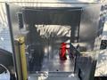 An empty metallic storage compartment with a red fire extinguisher inside and a yellow pole on the left