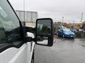 A 2008 Ford F-250 SD with a side mirror reflecting a blue car in the distance while rain droplets fall on its surface