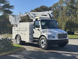 A white 2005 Freightliner M2 106 utility truck with an elevated work platform and multiple storage compartments on the sides