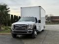 A white 2012 Ford F-550 truck with a boxy cargo bed and orange lights on the roof parked in a lot