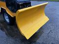A bright yellow snow plow blade with a curved design attached to a machinery unit with visible components and wheels